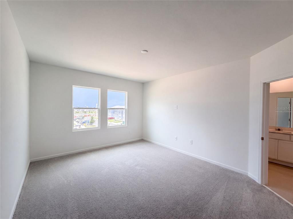 An empty bedroom with gray carpet, white walls, two windows, and an attached bathroom — 3102 KURTZ TERRACE, DAVENPORT, FL