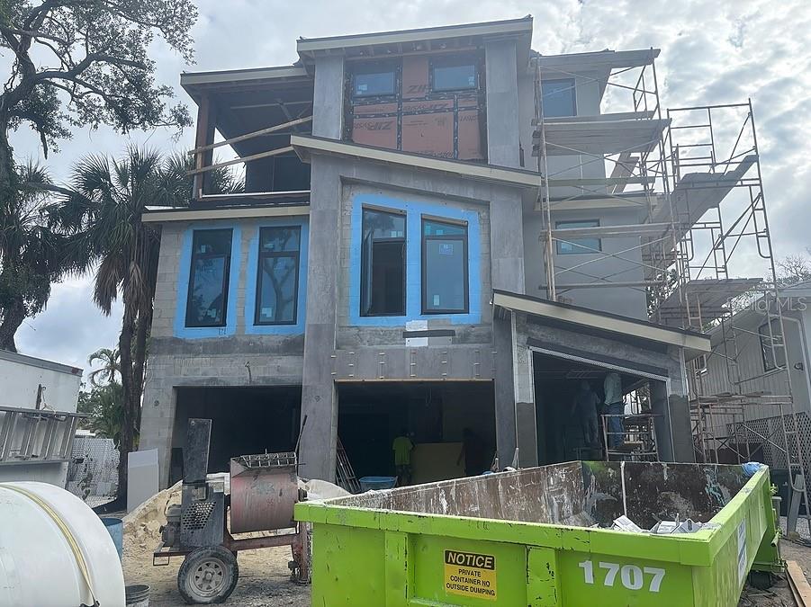 A three-story house under construction features concrete block walls, scaffolding, and a large green dumpster — 4903 COMMONWEALTH DRIVE, SARASOTA, FL