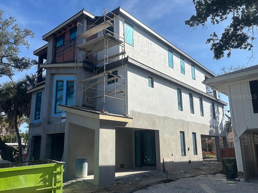 A three-story house under construction with scaffolding, stucco exterior, and a green dumpster — 4903 COMMONWEALTH DRIVE, SARASOTA, FL
