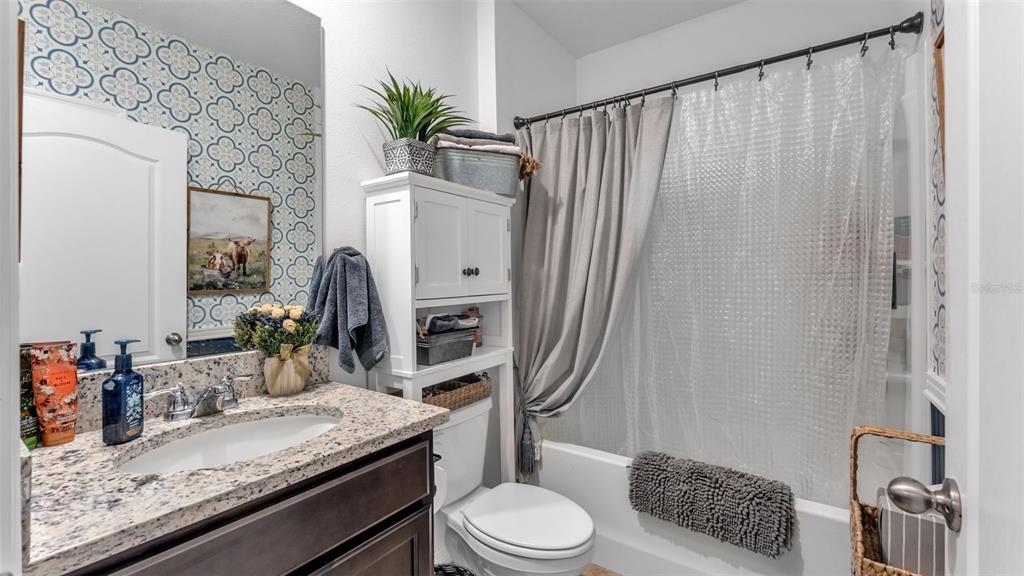 A bathroom features a granite vanity, patterned wallpaper, a white storage unit, and a shower curtain — 3612 DIVING DOVE LANE, BARTOW, FL