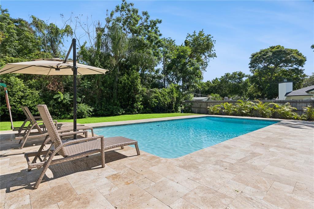 A rectangular swimming pool sits on a stone patio with lounge chairs and an umbrella — 2333 WESTMINSTER COURT, WINTER PARK, FL