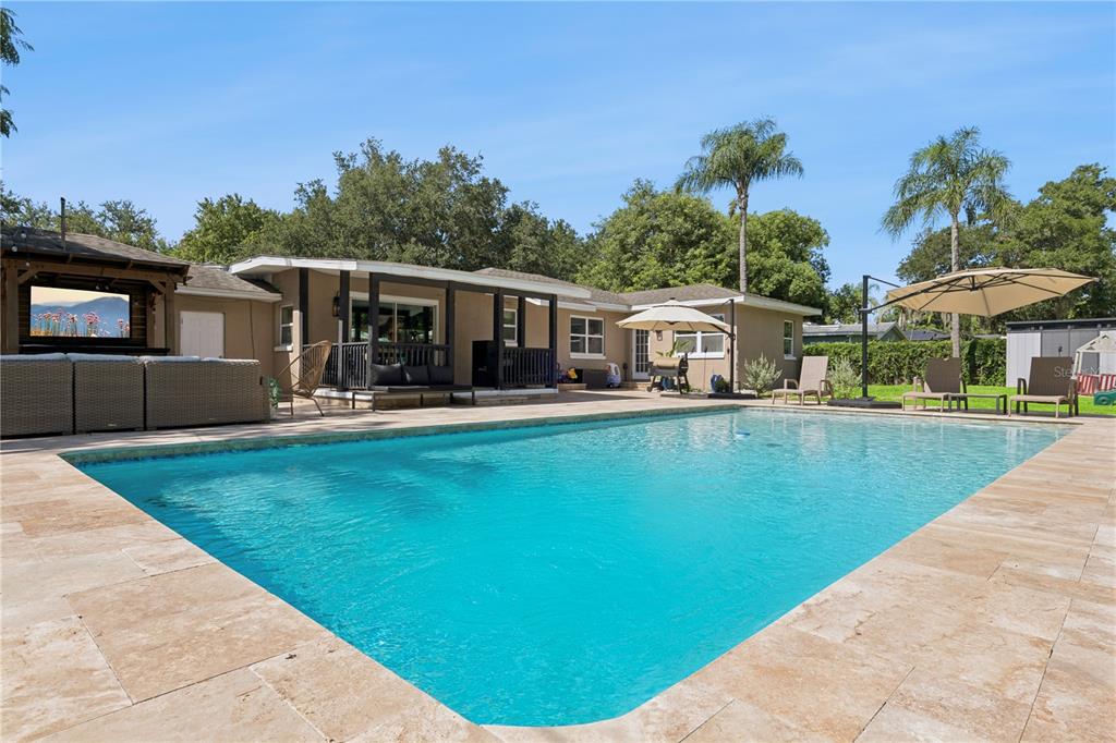A backyard features a rectangular swimming pool with stone decking, a covered patio, and landscaping — 2333 WESTMINSTER COURT, WINTER PARK, FL