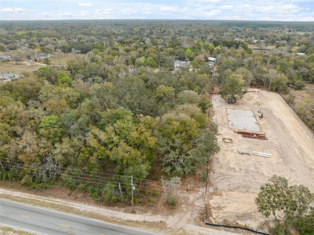 An aerial view shows a cleared construction site with a concrete foundation next to woods — 16308 SHADY HILLS ROAD, SPRING HILL, FL