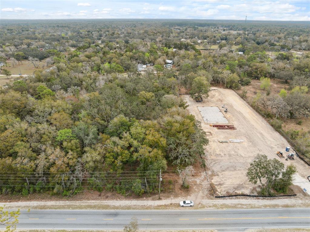 An aerial view shows a cleared construction site with a concrete foundation beside a wooded area — 16308 SHADY HILLS ROAD, SPRING HILL, FL