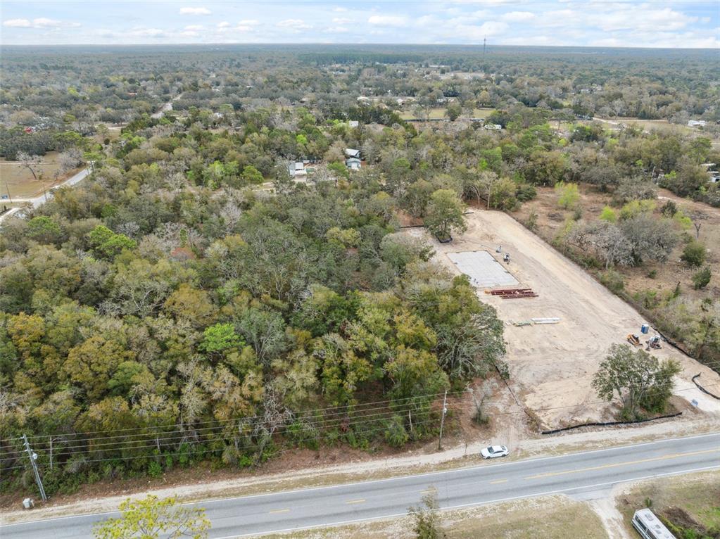 An aerial view shows a cleared construction site with a concrete foundation beside a wooded lot — 16308 SHADY HILLS ROAD, SPRING HILL, FL