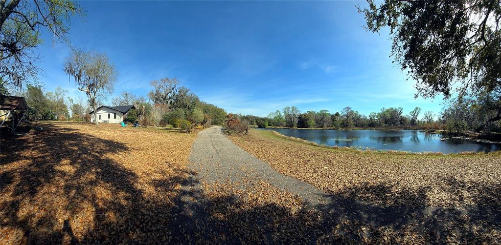 A gravel driveway leads past a house toward a pond on a tree-lined property — 14820 COUNTY ROAD 48, ASTATULA, FL