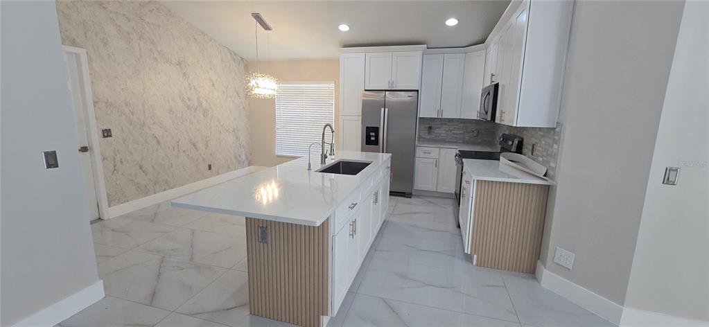 A modern kitchen features white cabinetry, a marble-patterned accent wall, and a light wood-paneled island — 600 ABACO COURT, KISSIMMEE, FL
