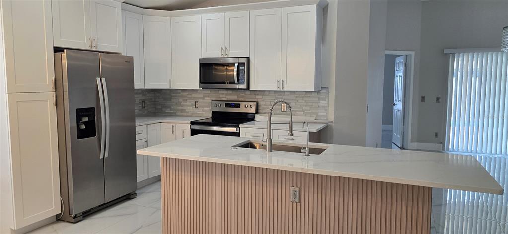 A kitchen features white cabinets, stainless steel appliances, a quartz-topped island, and a slatted base — 600 ABACO COURT, KISSIMMEE, FL