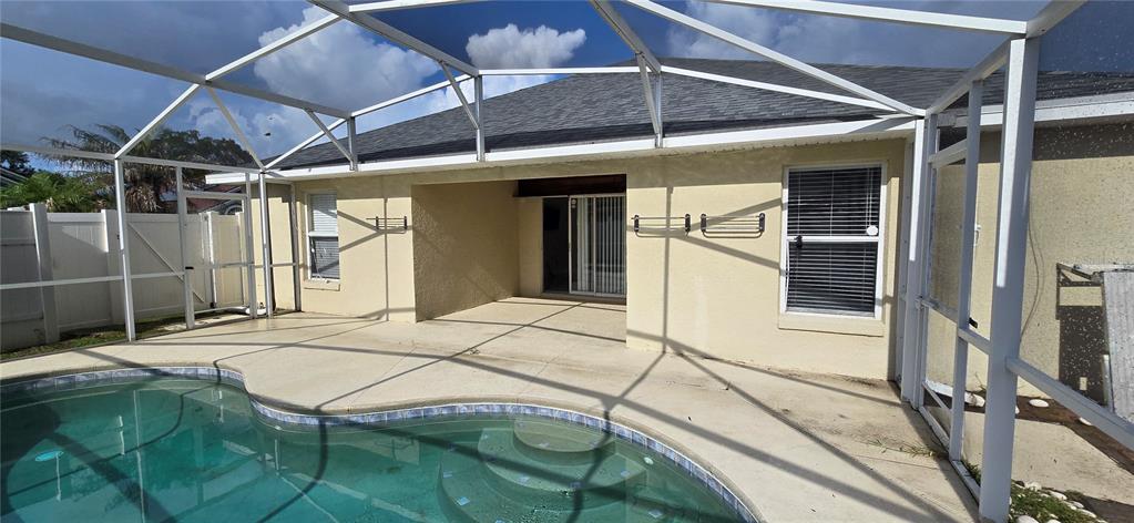 A swimming pool with a screened enclosure sits on a patio behind a stucco house — 600 ABACO COURT, KISSIMMEE, FL