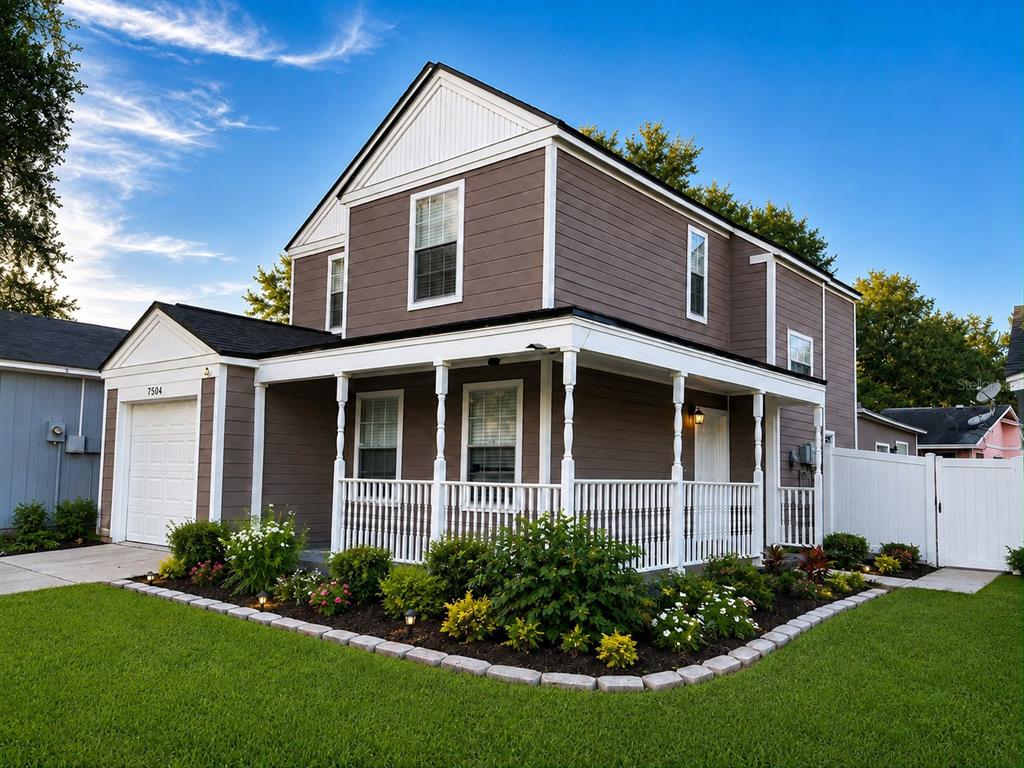 A two-story house with brown siding, a white porch, and a front-facing garage — 7504 GADSDEN DRIVE, TAMPA, FL