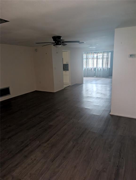 An open-concept living area features dark wood-look flooring, a ceiling fan, and a distant kitchen — 9436 GLEN MOOR LANE, PORT RICHEY, FL