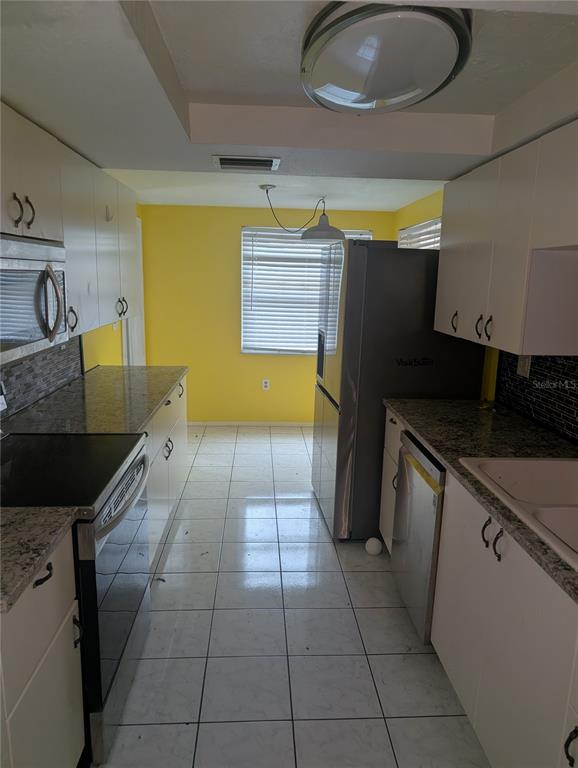 A galley kitchen features white cabinets, granite countertops, stainless steel appliances, and yellow accent walls — 9436 GLEN MOOR LANE, PORT RICHEY, FL