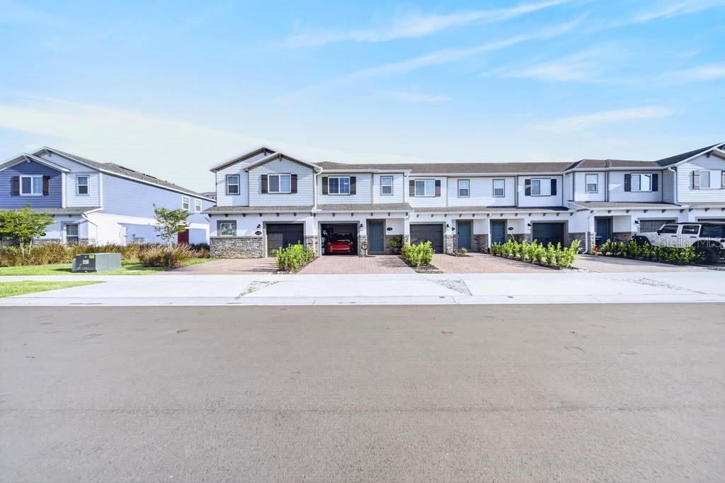 A row of modern two-story townhouses with attached garages and paved driveways under a blue sky — 4176 CAMPSITE LOOP, ORLANDO, FL