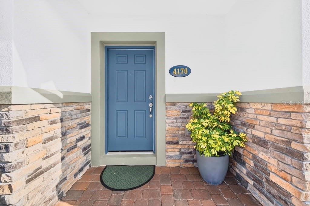 A blue front door is set within a stone-accented entryway with a potted plant — 4176 CAMPSITE LOOP, ORLANDO, FL