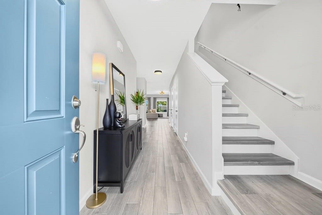A bright entryway features a blue door, a black console table, and stairs with wood treads — 4176 CAMPSITE LOOP, ORLANDO, FL