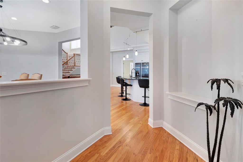 A hallway with hardwood floors leads to a kitchen with a breakfast bar and stools — 1215 LAKESHORE DRIVE, EUSTIS, FL