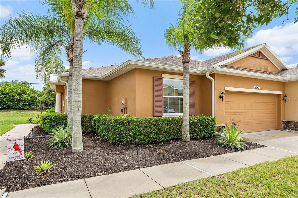 A tan single-story house with a two-car garage, palm trees, and a landscaped front yard — 11547 52ND COURT E, PARRISH, FL