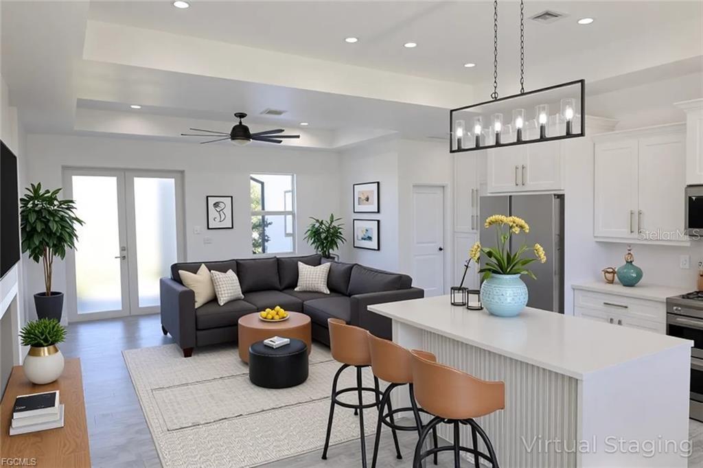 This open-concept living room and kitchen features white cabinetry, a gray sectional, and island seating — 114 PRESTON STREET, LEHIGH ACRES, FL