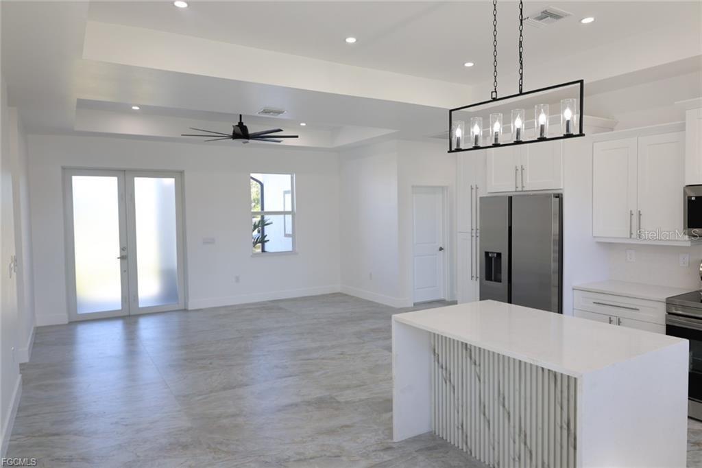 A modern kitchen and living area feature white cabinetry, a marble-accented island, and tile flooring — 114 PRESTON STREET, LEHIGH ACRES, FL
