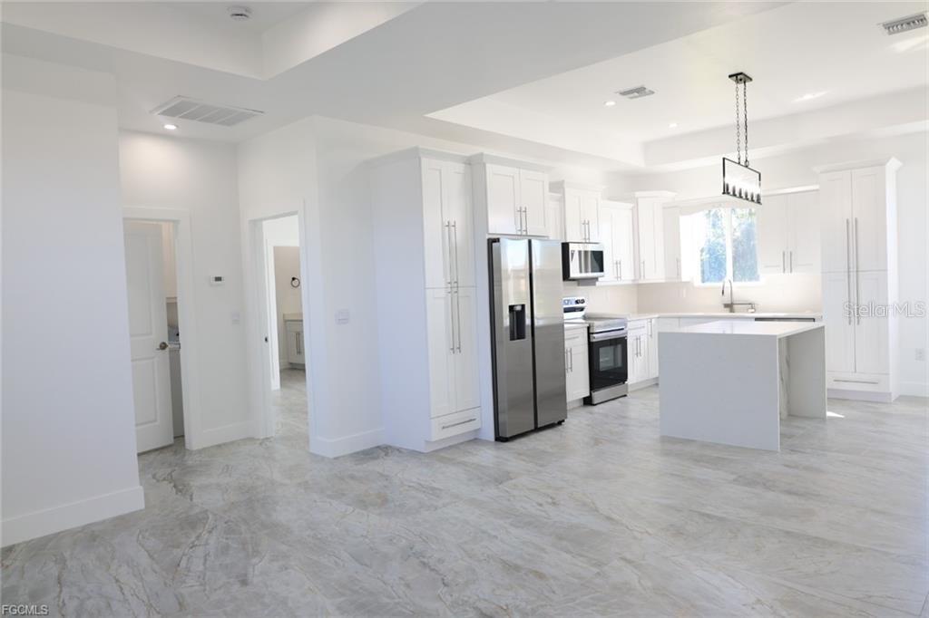 A modern kitchen features white cabinetry, stainless steel appliances, a center island, and marble flooring — 114 PRESTON STREET, LEHIGH ACRES, FL