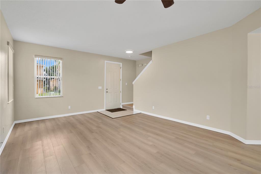 An empty living room features light-colored wood-look flooring, beige walls, and a front entry door — 822 KETTERING ROAD, DAVENPORT, FL