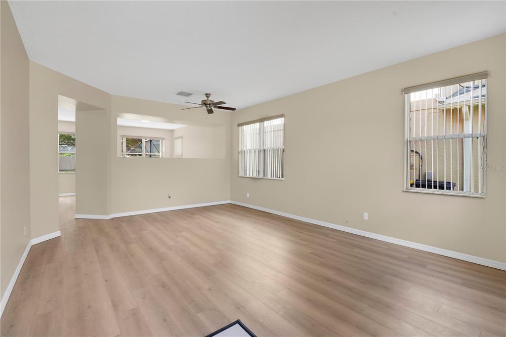 An empty living room features light-colored walls, wood-look flooring, a ceiling fan, and two windows — 822 KETTERING ROAD, DAVENPORT, FL