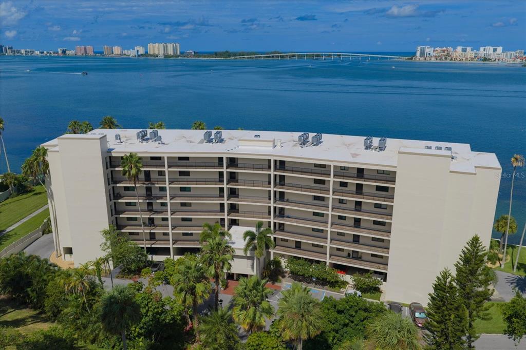 An aerial view of a multi-story apartment building situated along a waterfront with a bridge — 55 ROGERS STREET UNIT P3, CLEARWATER, FL