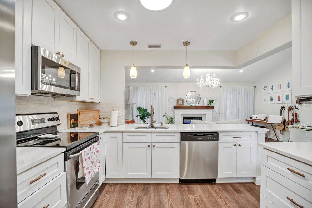 A kitchen with white cabinets, stainless steel appliances, and a peninsula overlooking a living room — 2958 MALLORN WAY, CASSELBERRY, FL
