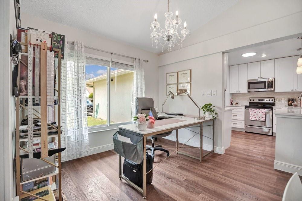 A home office with a desk, chandelier, and window, adjacent to a kitchen with white cabinets — 2958 MALLORN WAY, CASSELBERRY, FL