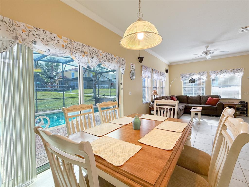 A dining area with a wooden table overlooks a backyard pool through sliding glass doors — 8535 BAY LILLY LOOP, KISSIMMEE, FL
