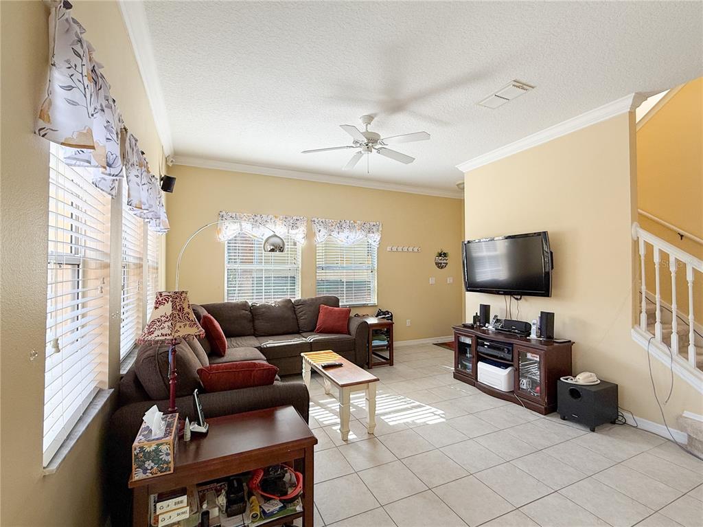 A living room features tile flooring, a brown sectional sofa, a television, and a staircase — 8535 BAY LILLY LOOP, KISSIMMEE, FL