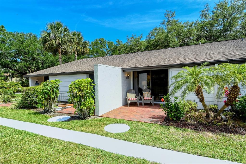 A ground-level patio with two chairs sits in front of a single-story residential building — 3545 LONGMEADOW UNIT 23, SARASOTA, FL