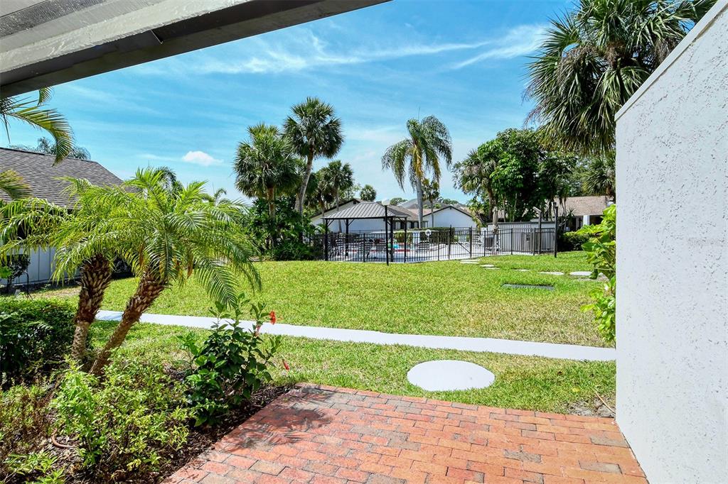 A view from a brick patio looking out toward a grassy lawn and community pool — 3545 LONGMEADOW UNIT 23, SARASOTA, FL