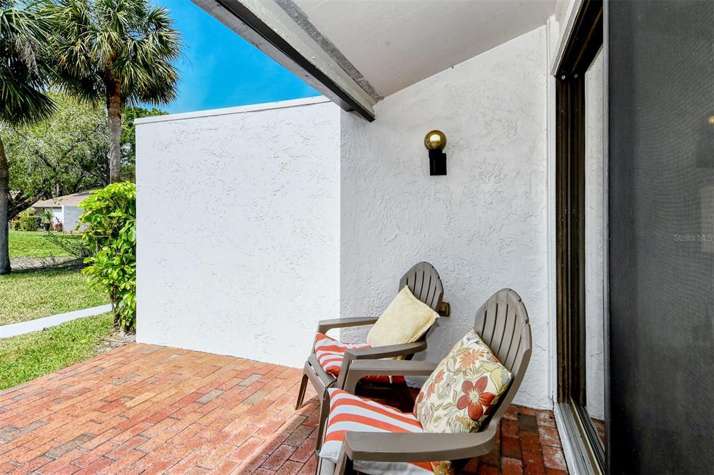 A brick patio features two chairs against a white wall with an outdoor light fixture — 3545 LONGMEADOW UNIT 23, SARASOTA, FL