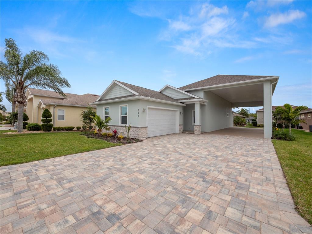 A light green house with a paved driveway, a one-car garage, and a side carport — 715 TEABERRY TRAIL, POLK CITY, FL