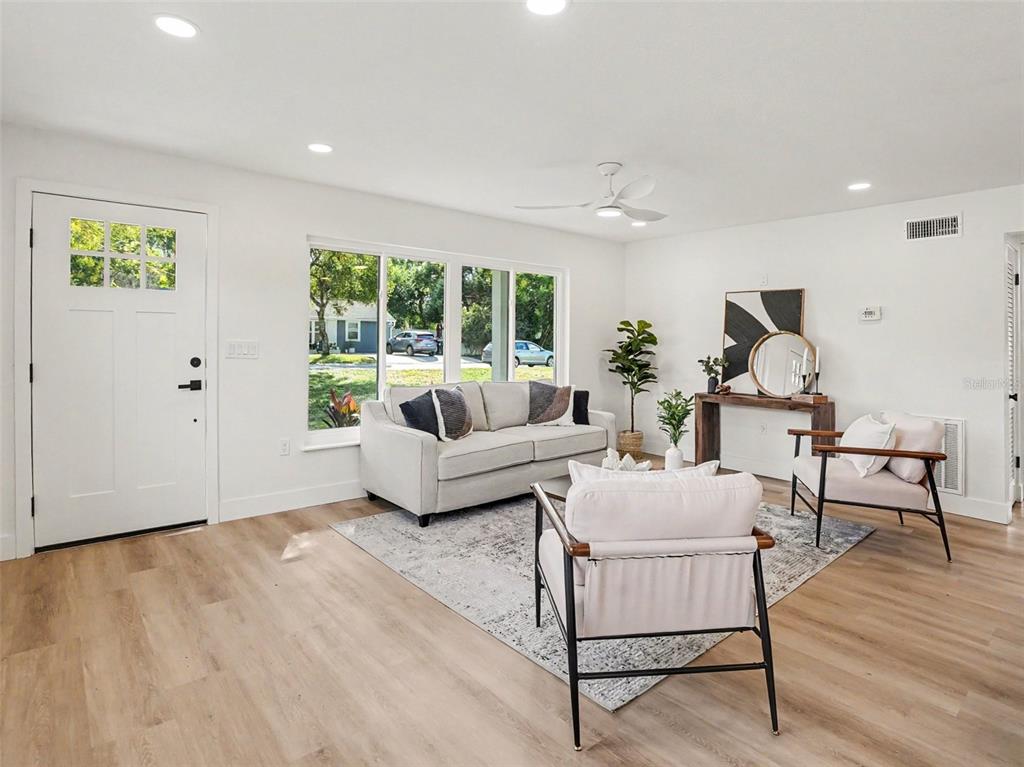 A bright living room features light wood flooring, a white sofa, and two accent chairs — 2400 REST HAVEN AVENUE, ORLANDO, FL