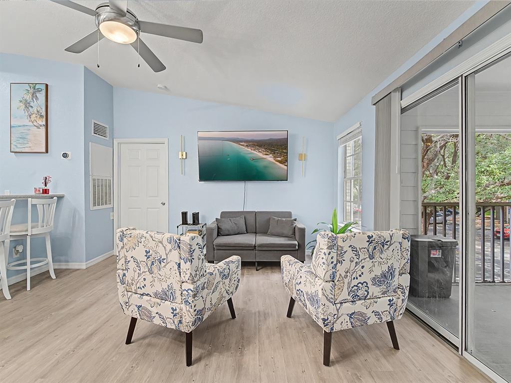 A living room features light blue walls, wood-look flooring, a ceiling fan, and two patterned armchairs — 5112 PARK CENTRAL DRIVE UNIT 621, ORLANDO, FL