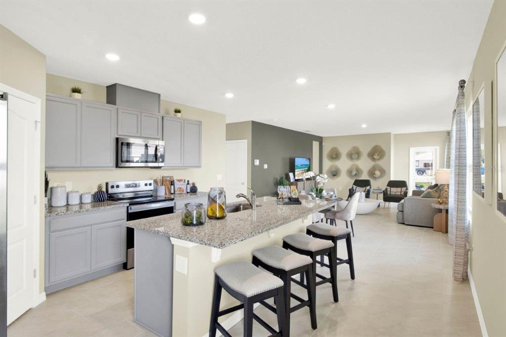 A kitchen with gray cabinets and granite countertops opens into a living area with seating — 4160 GIORGIO DRIVE, WINTER HAVEN, FL