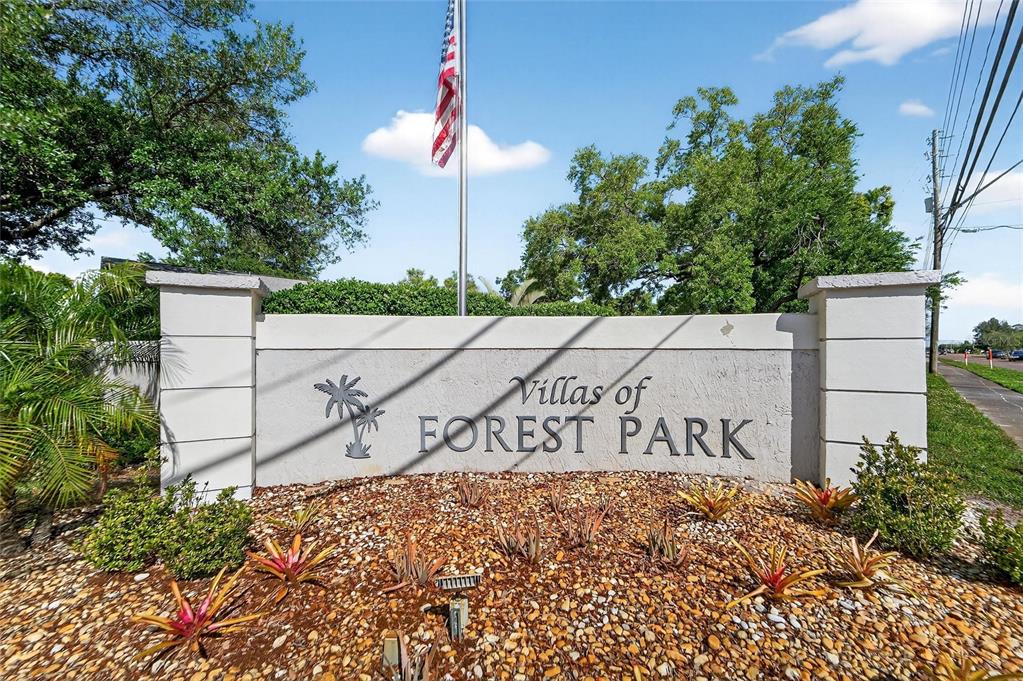 A stone monument sign for Villas of Forest Park stands in a landscaped garden area — 2369 BEVERLY DRIVE, DUNEDIN, FL