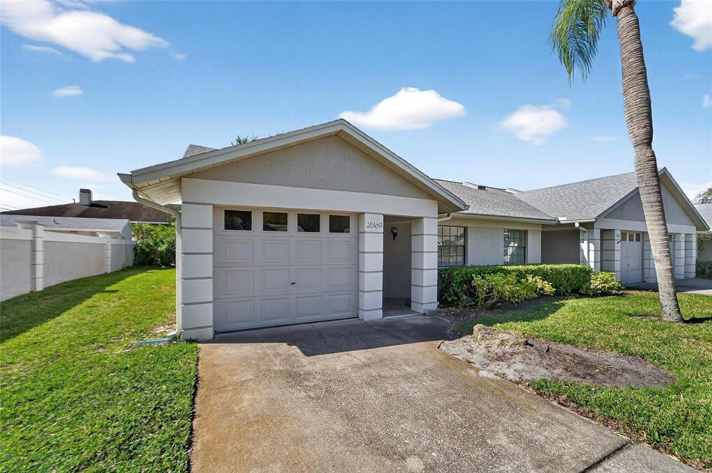 A single-story house exterior features a beige stucco facade, a garage, and a palm tree — 2369 BEVERLY DRIVE, DUNEDIN, FL