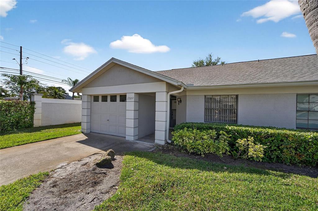 A single-story house exterior features a one-car garage, a covered entryway, and landscaped bushes — 2369 BEVERLY DRIVE, DUNEDIN, FL