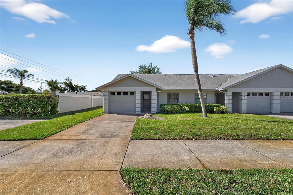 A single-story duplex with two garages, a concrete driveway, and a palm tree in front — 2369 BEVERLY DRIVE, DUNEDIN, FL