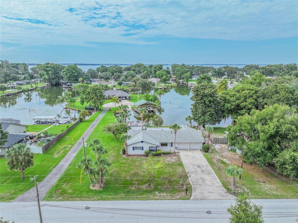 An aerial view shows a single-story house with a driveway and lawn bordering a lake — 2712 GRAND ISLAND SHORES ROAD, EUSTIS, FL