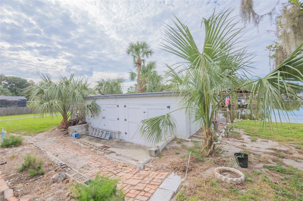 A white concrete block storage building sits in a yard near a canal with palm trees — 2712 GRAND ISLAND SHORES ROAD, EUSTIS, FL