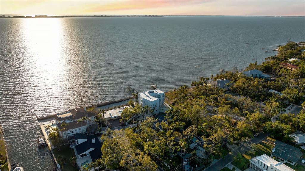 An aerial view shows a white waterfront home surrounded by trees along a large bay — 2046 ALAMEDA AVENUE, SARASOTA, FL