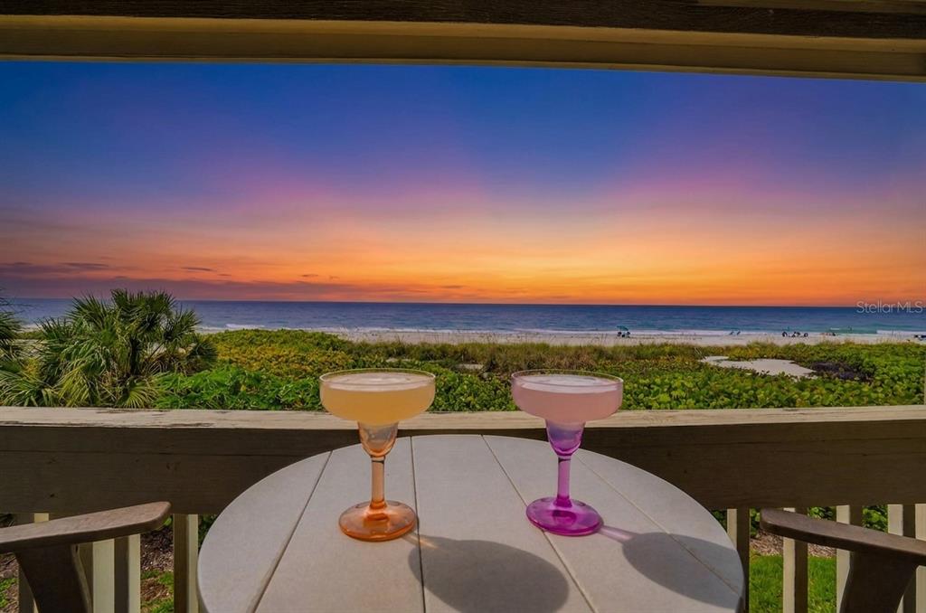 Two cocktails sit on a balcony table overlooking a beach at sunset — 5275 GULF OF MEXICO DRIVE UNIT 202, LONGBOAT KEY, FL