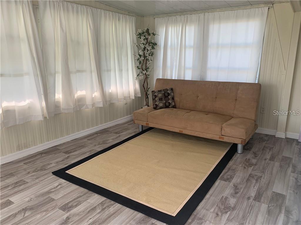 A sunroom features light wood-look flooring, white curtains, a tan futon, and a neutral area rug — 10 BOCA CIEGA, NOKOMIS, FL
