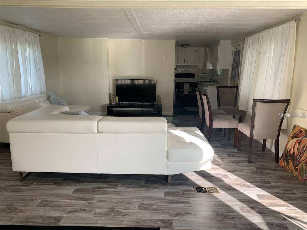 A living room with a white sectional sofa, television, and dining area with wood-look flooring — 10 BOCA CIEGA, NOKOMIS, FL