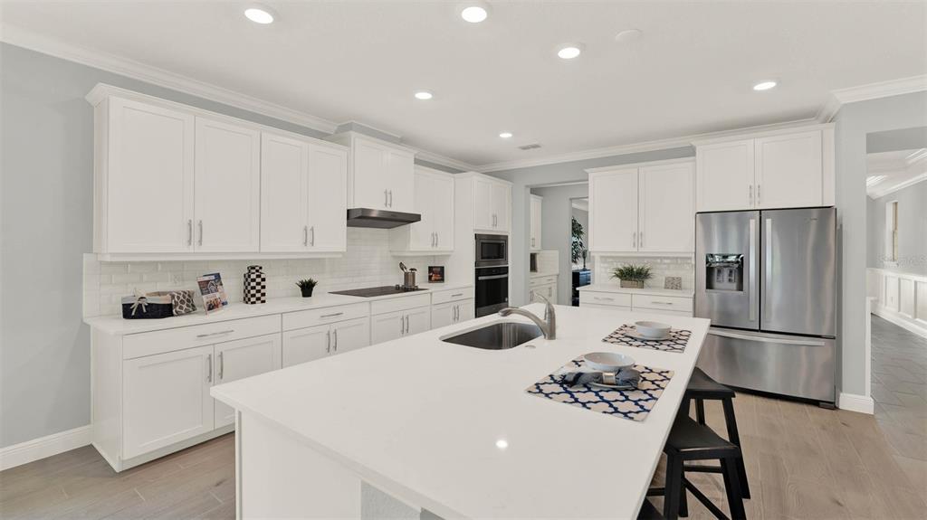 A modern kitchen features white cabinets, a central island with a sink, and stainless appliances — 11845 SHINE VIEW LANE, WINTER GARDEN, FL