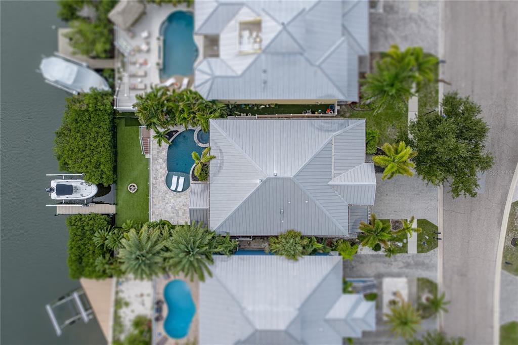 An aerial view shows a waterfront house with a metal roof, pool, and boat dock — 6411 GRENADA ISLAND AVENUE, APOLLO BEACH, FL